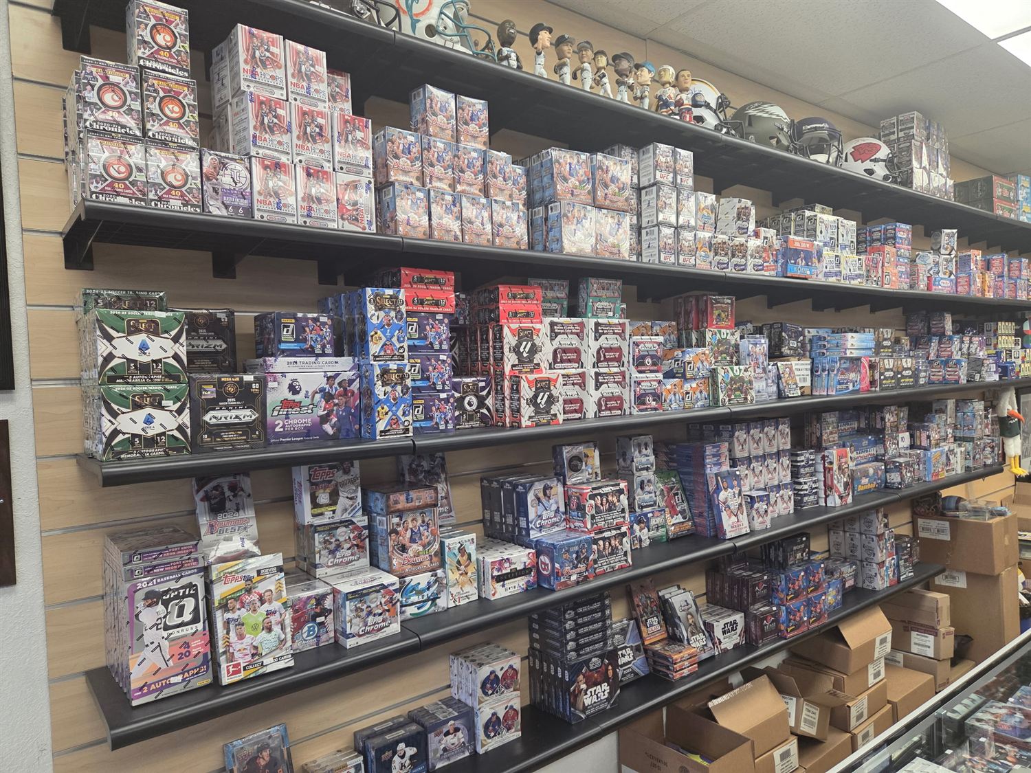 Sports card wall — NBA, Bowman, UFC and soccer boxes with helmets and bobbleheads